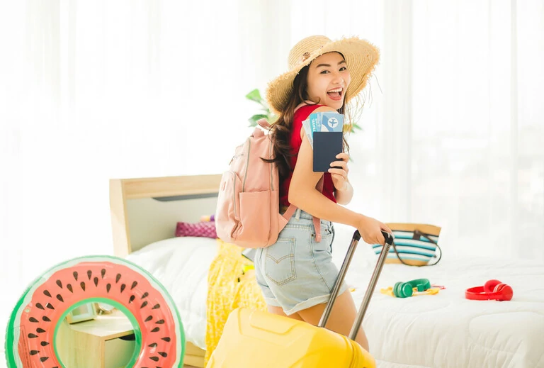Happy asiatische Frau lächeln, während sie zeigen Pass und Flugticket mit vielen Gegenständen, um auf Reisen Strand Reise am Wochenende vorzubereiten. Junge hübsche Frau mit Koffer, die in den Urlaub fahren wird.
